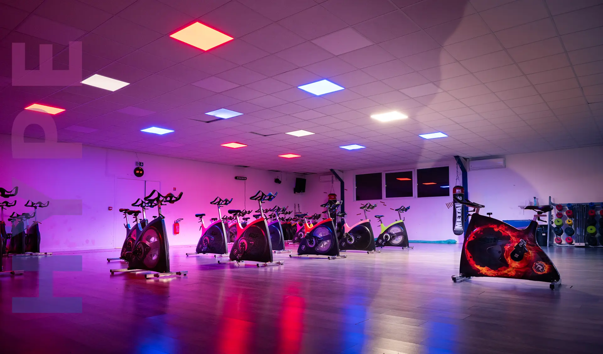 Salle des cours collectifs éclairée en rose et bleu avec vélos de biking